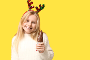 Happy little girl in reindeer horns with chocolate Santa Claus on yellow background