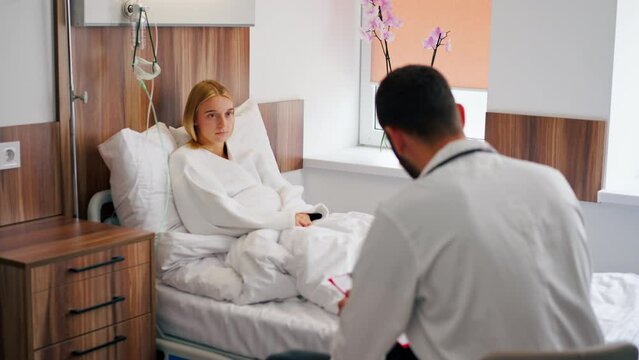 A sick girl lies in hospital room and holds her chest with her hand and coughs near the doctor