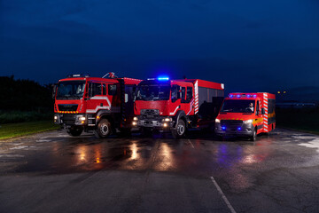 A pair of highly modern and quality fire trucks illuminate the night with their rotating lights,...