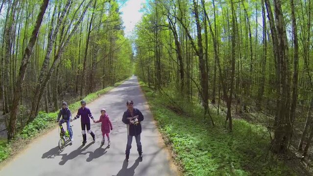 family ride on rollerskates and bike by road along forest 
