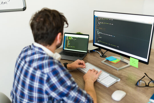 Hispanic programmer typing and writing a new code on the computer while working at the office coding developing new software