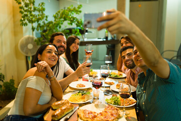 Group of happy friends enjoying having dinner together and talking a selfie