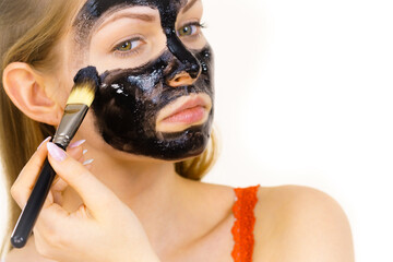 Woman applying black mask to skin face