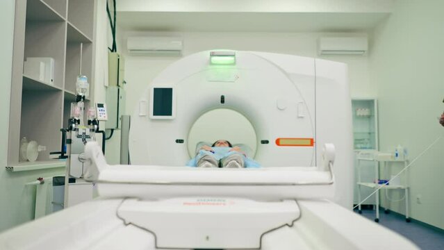 A girl in a medical gown lies on a movable couch of a magnetic resonance imaging machine and prepares for diagnosis
