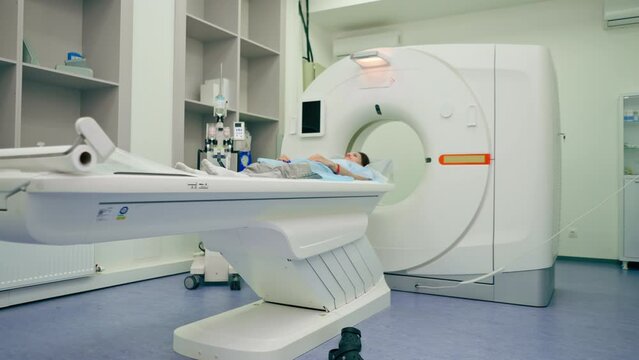 A girl in a medical gown lies on a movable couch of a magnetic resonance imaging machine and prepares for diagnosis