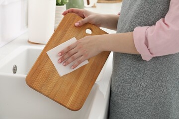 Woman wiping wooden cutting board with paper napkin at sink in kitchen, closeup