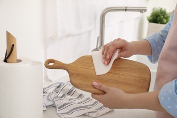 Woman wiping wooden cutting board with paper napkin in kitchen, closeup