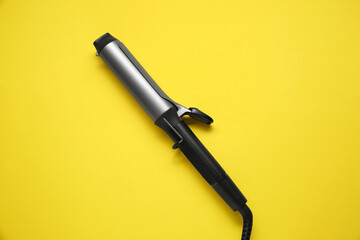 Hair curling iron on yellow background, top view