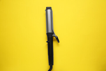 Hair curling iron on yellow background, top view