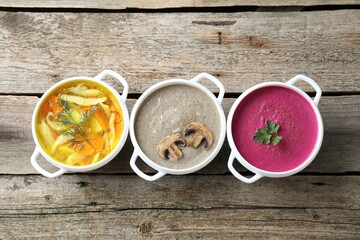 Tasty broth and cream soups in bowls on old wooden table, flat lay