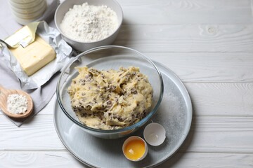 Chocolate chip cookie dough in bowl and ingredients on white wooden table