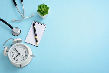 Stethoscope, clock, pen, notebook, and greenery on a blue background