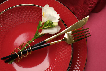 Stylish table setting with cutlery and floral decor on pink background, top view