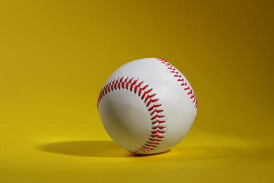 One baseball ball with stitches on yellow background