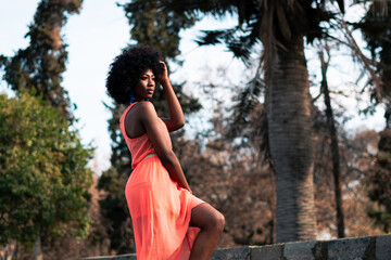 beautiful black woman with orange dress enjoying a sunny day, full, thoughtful and melancholic in a park in the city