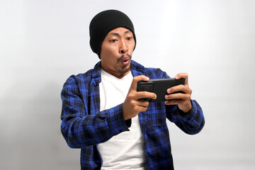 an Annoyed Asian man, dressed in a beanie hat and casual shirt, displays frustration and disappointment after losing while playing an online mobile game on his phone, appearing shocked by the outcome