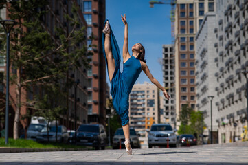 Beautiful Asian ballerina in blue dress posing in splits outdoors. Urban landscape.