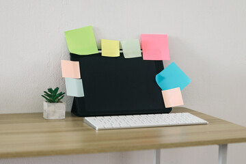 Blank multicolor sticky notes on laptop screen at office desk