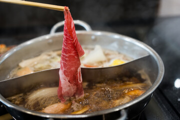 Man hand takes raw delicious beef sliced of high quality with put cooking in hot boiled soup with vegetable in the restaurant.