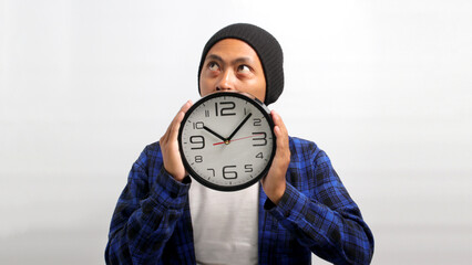 Asian man, dressed in a beanie hat and casual shirt, appears to be deep in thought and planning as...