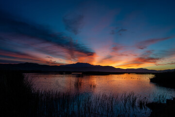 Obraz premium The orange and blue hues of sunrise over a lake with beautiful reflections of a hill and colors