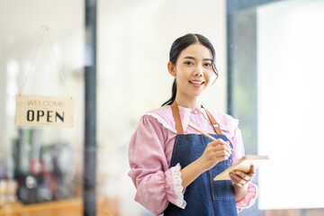 Portrait of happy waitress standing at restaurant entrance. SME entrepreneur young business asian woman attend new customers near door. Smiling small business owner showing open sign in her shop.