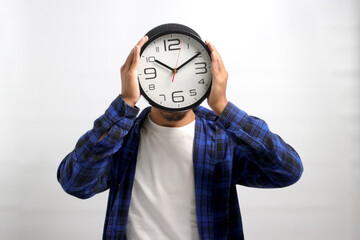 Asian man, dressed in beanie hat and casual shirt, creatively uses a clock to cover his head or...