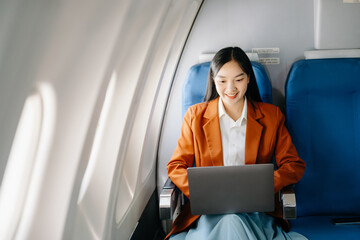 Asian executive excels in first class, multitasking with digital tablet, laptop. Travel in style,...