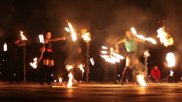 Two girls move with burning fans and four guys rotate pois, staff