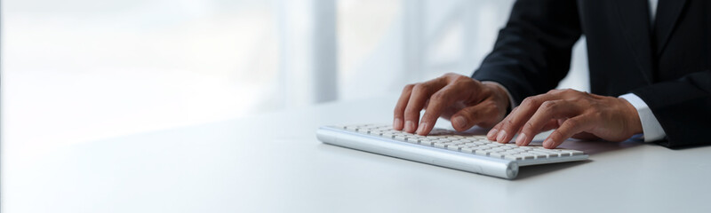 Cropped view of businessman typing on keyboard Hand typing on wireless computer keyboard and mouse in office, writing, typing email or communicating online. copy space, banner , panorama