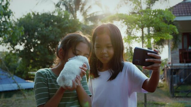 Two asian girls taking a picture and playing with baby bunny.