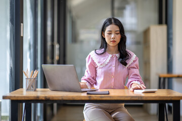 Fototapeta premium Photo of cheerful joyful young asian business woman in the office working on laptop digital project sitting at desk.