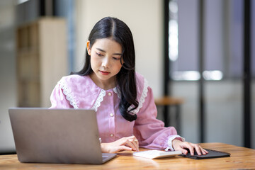 Photo of cheerful joyful young asian business woman in the office working on laptop digital project sitting at desk.