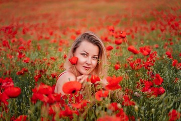 Obraz na płótnie Canvas Happy woman in a red dress in a beautiful large poppy field. Blond sits in a red dress, posing on a large field of red poppies
