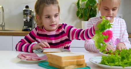 Two little girls making sandwiches on the kitchen.