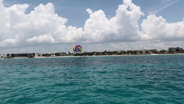 Panor&aacute;mico de un paraca&iacute;das con los colores LGBTQ+ levantando el vuelo sobre el mar.