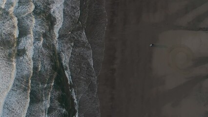 Aerial overhead view of a truck driving on the beach next to the ocean.