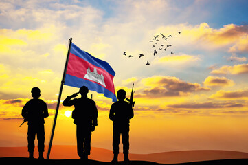 Silhouettes of soldiers with the Cambodia flag stand against the background of a sunset or sunrise....