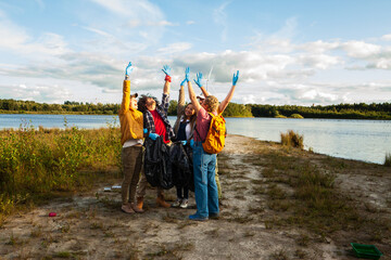 This uplifting image portrays a group of four volunteers, two women and two men, celebrating their successful clean-up at a lake. They are diverse in age and ethnicity, including a young Caucasian man