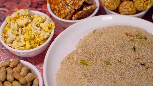 Beautifully served Lohri items consumed on the Lohri festival during wintertime. Closeup shot of a plate surrounded by popcorns  murmure laddoo  peanuts chikki  bhujia chikki  and til patti