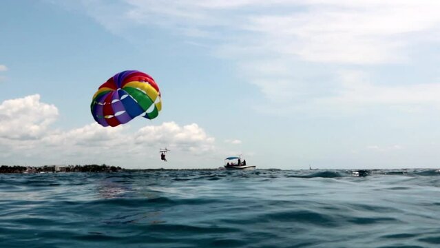 Panor&aacute;mico de un paraca&iacute;das con los colores LGBTQ+ levantando el vuelo sobre el mar.