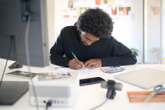 Concentrated Project Development.  Black man writing notes in a bright creative office.