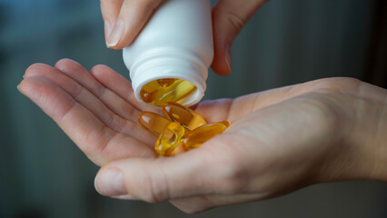Close-up of a woman pouring vitamin D or omega-3 into her hand. Healthcare and medicine, well-being...