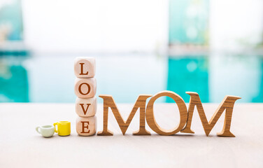 Mom wooden font with love wooden cube and coffee cup on swimming pool edge, mother's day card...