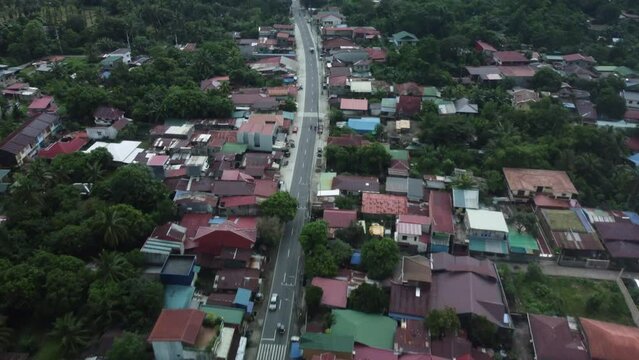 Drone shot of Provincial Philippine highway, with cars moving, surrounded by trees and small houses