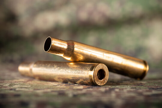 Two rifle bullets cartridges on green military camouflage fabric texture background
