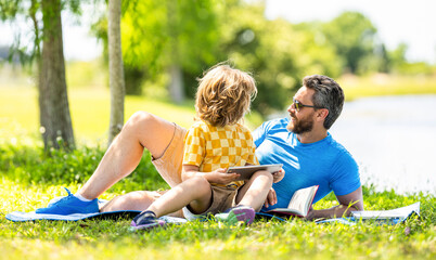 Father and son child relax in park. childhood school education. son with father bonding in summer. education of father and son kid. Father shapes son education with book and tablet. learn outdoor