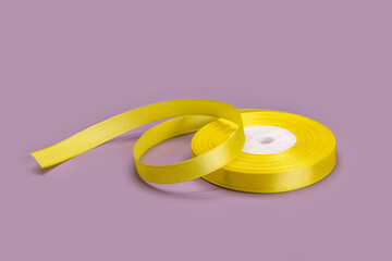 A roll of yellow satin ribbon for gift wrapping. Studio shot, lilac background.