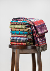 Neatly folded on a chair are stacks of cashmere stoles, shawls, scarves of different colors. Women's accessory, gift souvenir, gray background.