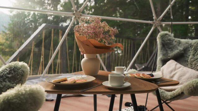 Breakfast on glamping cottage glass terrace. Low table paired with fluffy armchairs creates calm atmosphere to rest with stunning views. Perfect morning